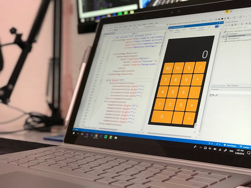 A close-up view of a laptop on a desk displaying lines of HTML code on the screen alongside a large, orange calculator application. The environment appears to be a modern workspace with a blurred back